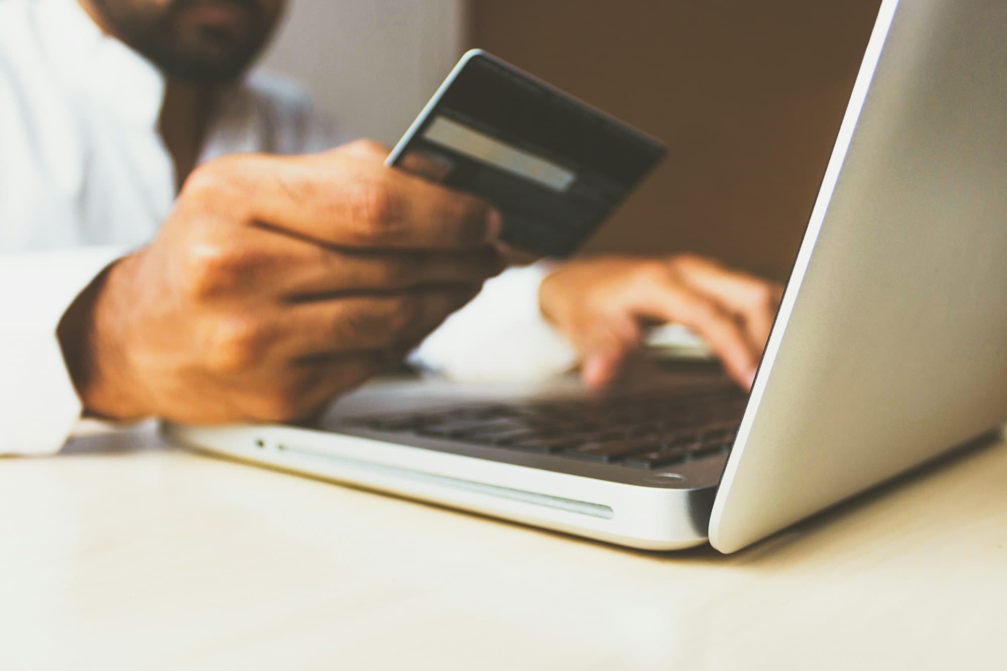 Hand holding a payment card next to an open laptop